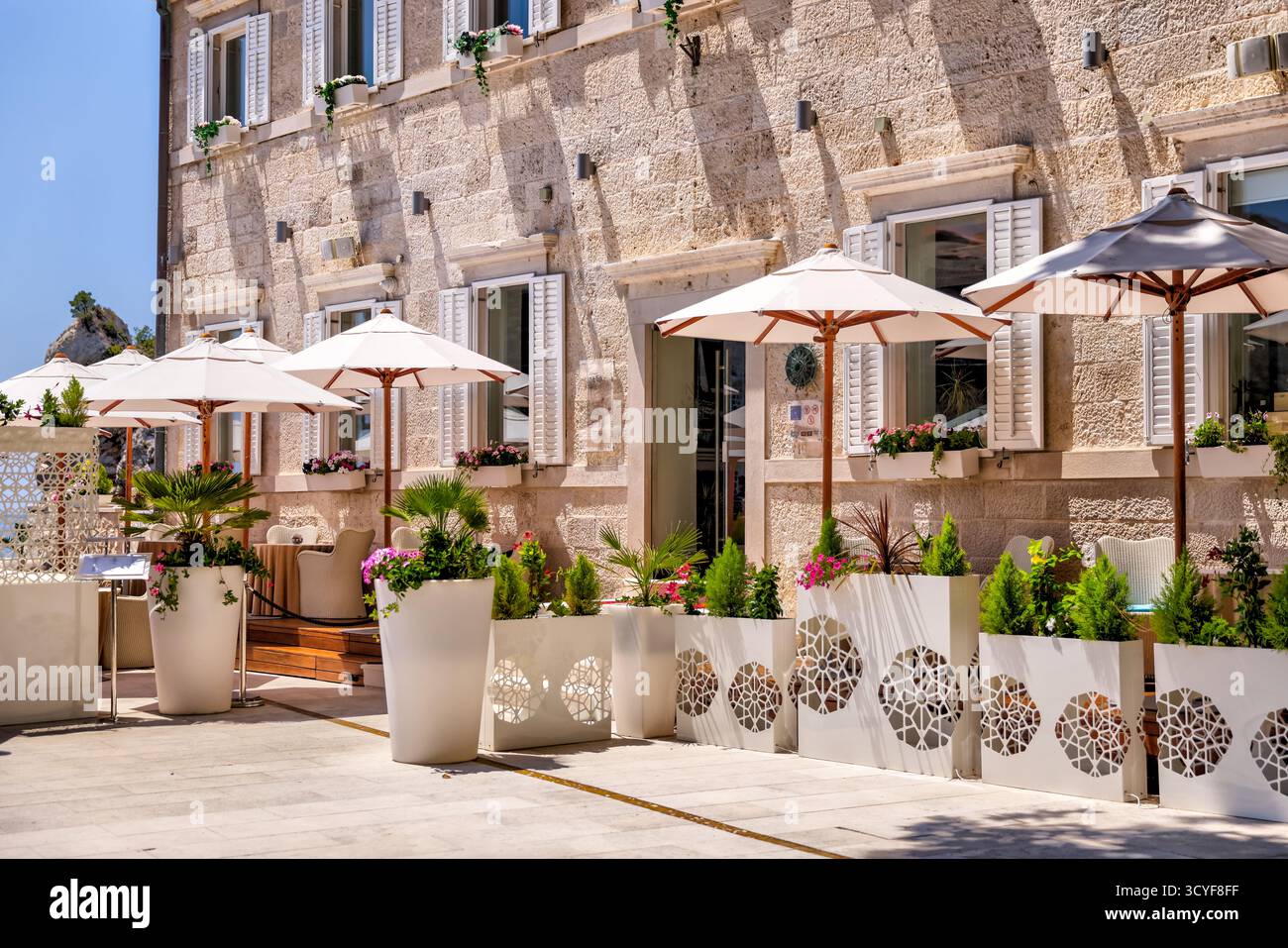 Situé à Dubrovnik, en Croatie, le café-terrasse en bord de mer avec des parasols blancs offre une vue sur l'océan et propose des repas en plein air le long de la côte Adriatique. Banque D'Images