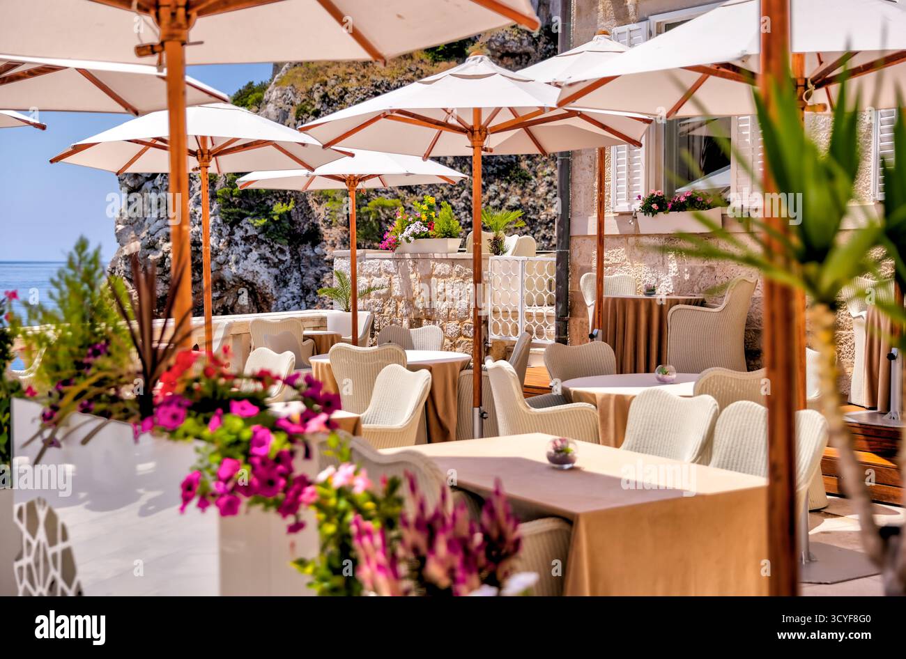 Situé à Dubrovnik, en Croatie, le café-terrasse en bord de mer avec des parasols blancs offre une vue sur l'océan et propose des repas en plein air le long de la côte Adriatique. Banque D'Images