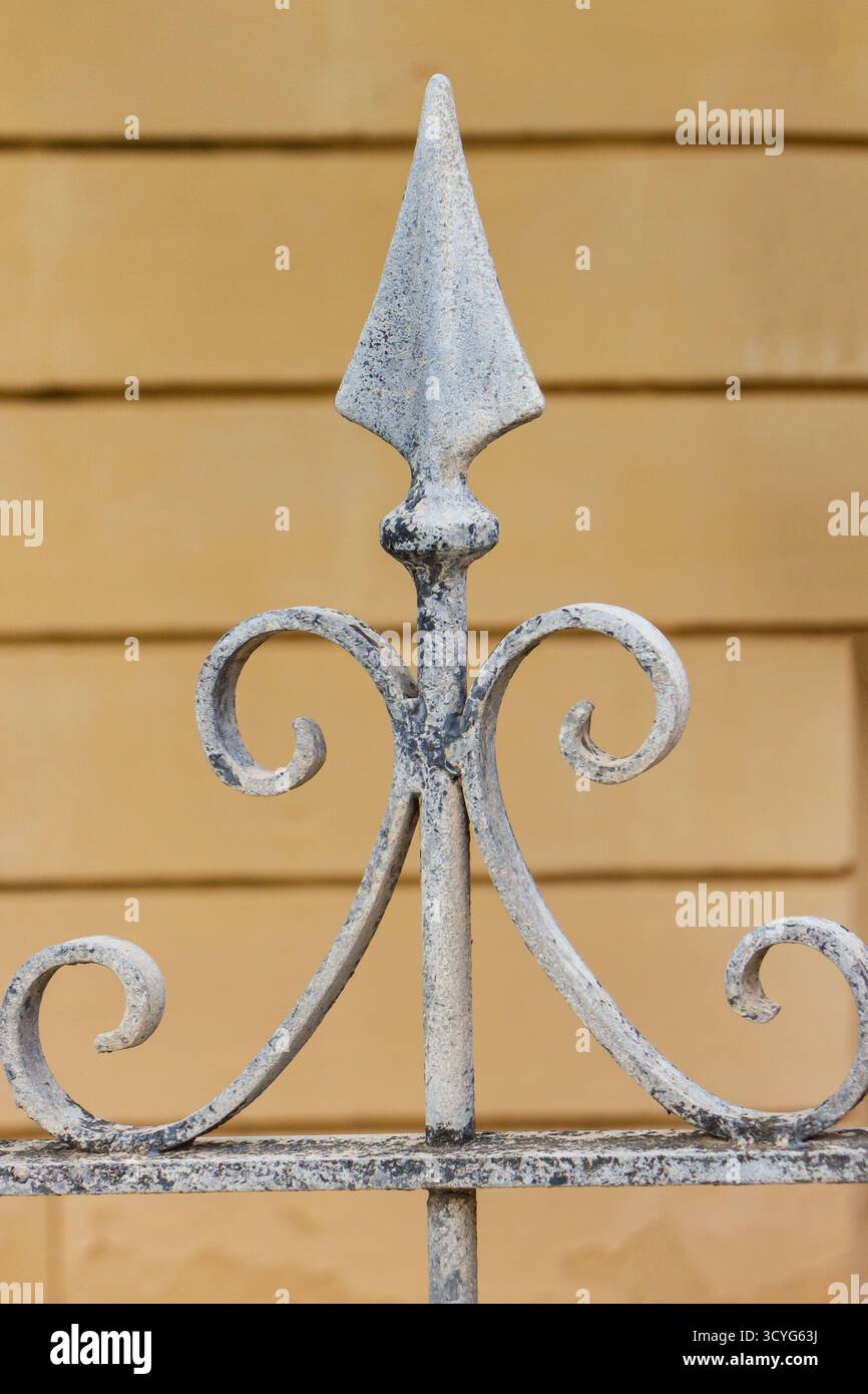 Finition de clôture décorative en fer forgé avec volutes et pointes de lance contre mur jaune Banque D'Images