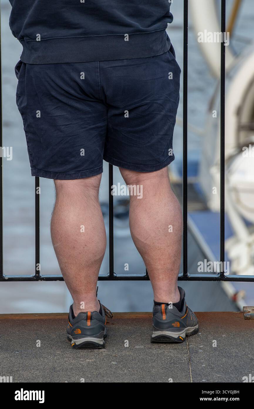 Vue arrière en surpoids de l'homme portant un short homme avec de grands muscles du mollet avec vue arrière. Gros muscles de jambe sur l'homme en surpoids en short bleu Banque D'Images