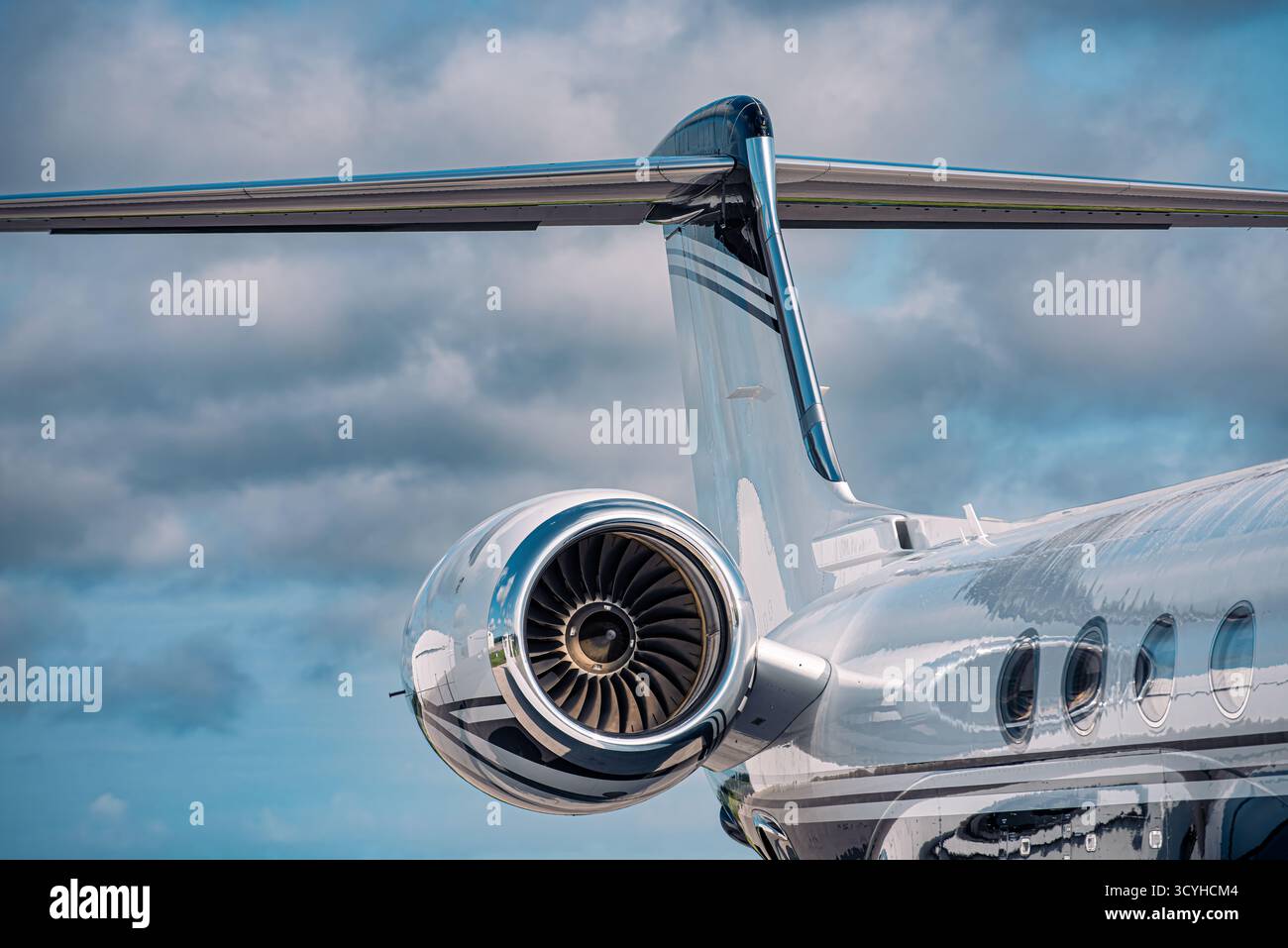 Gros plan d'un moteur à réaction poli et d'une queue en T sur un jet d'affaires moderne, reflétant le ciel sombre au-dessus de la rampe d'accès de l'aéroport. Banque D'Images