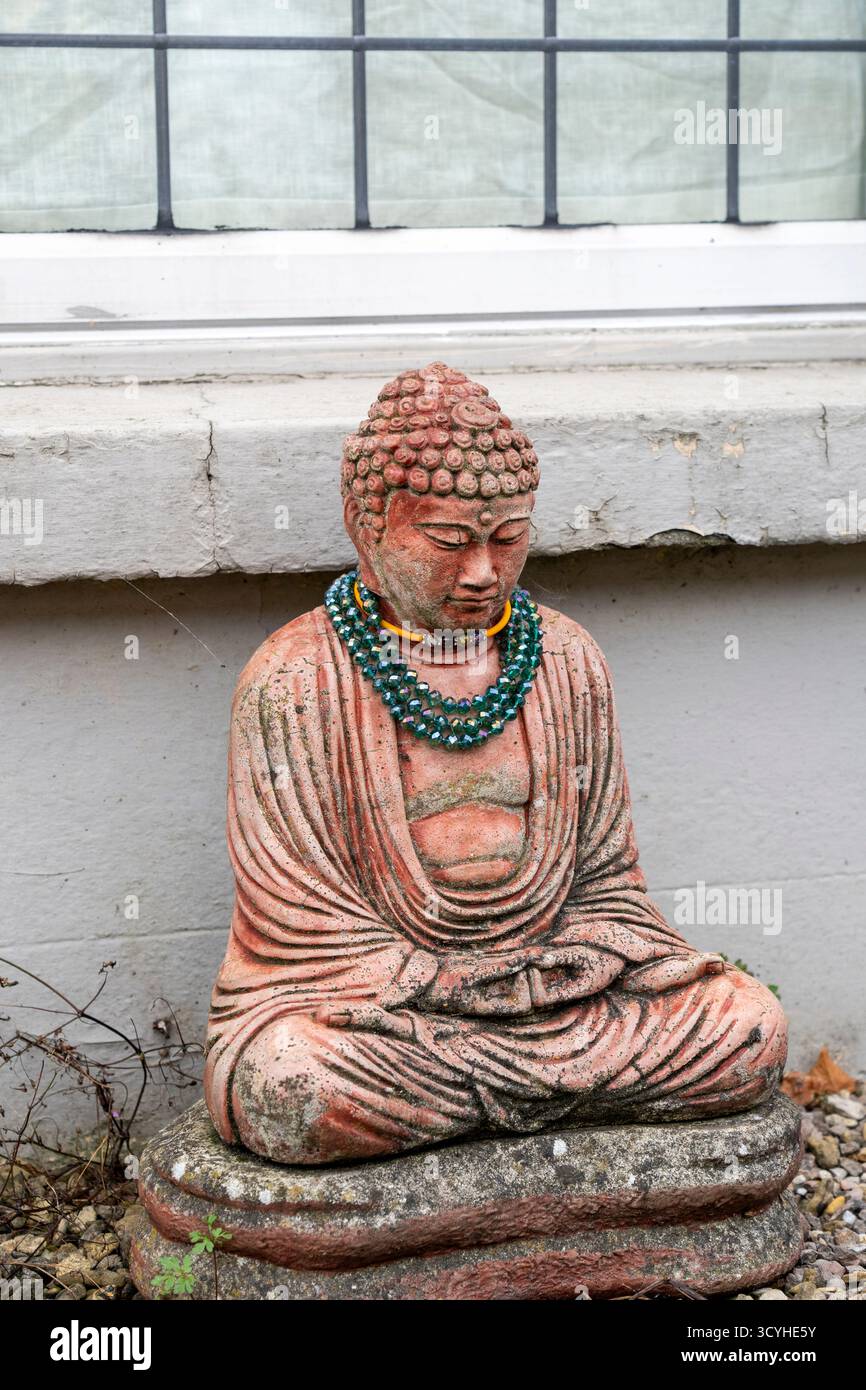 Figurine de Bouddha portant un collier assis sous une fenêtre Banque D'Images