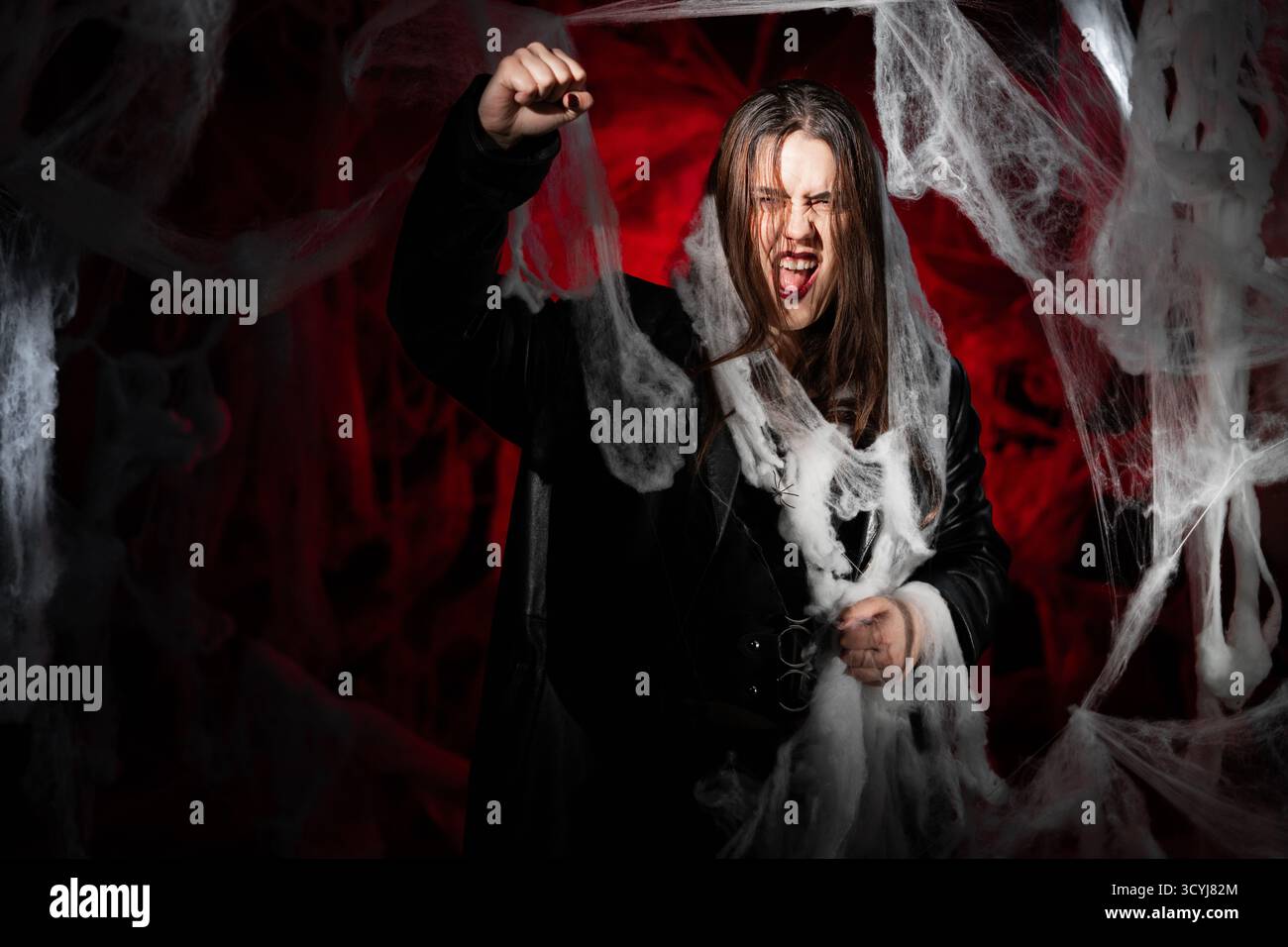 femme gothique avec le maquillage vampire effrayant piégé dans la toile d'araignée essayant d'effrayer montrant le geste de grève et poing-up. Fantaisie effrayante fille sur halloween rouge Banque D'Images
