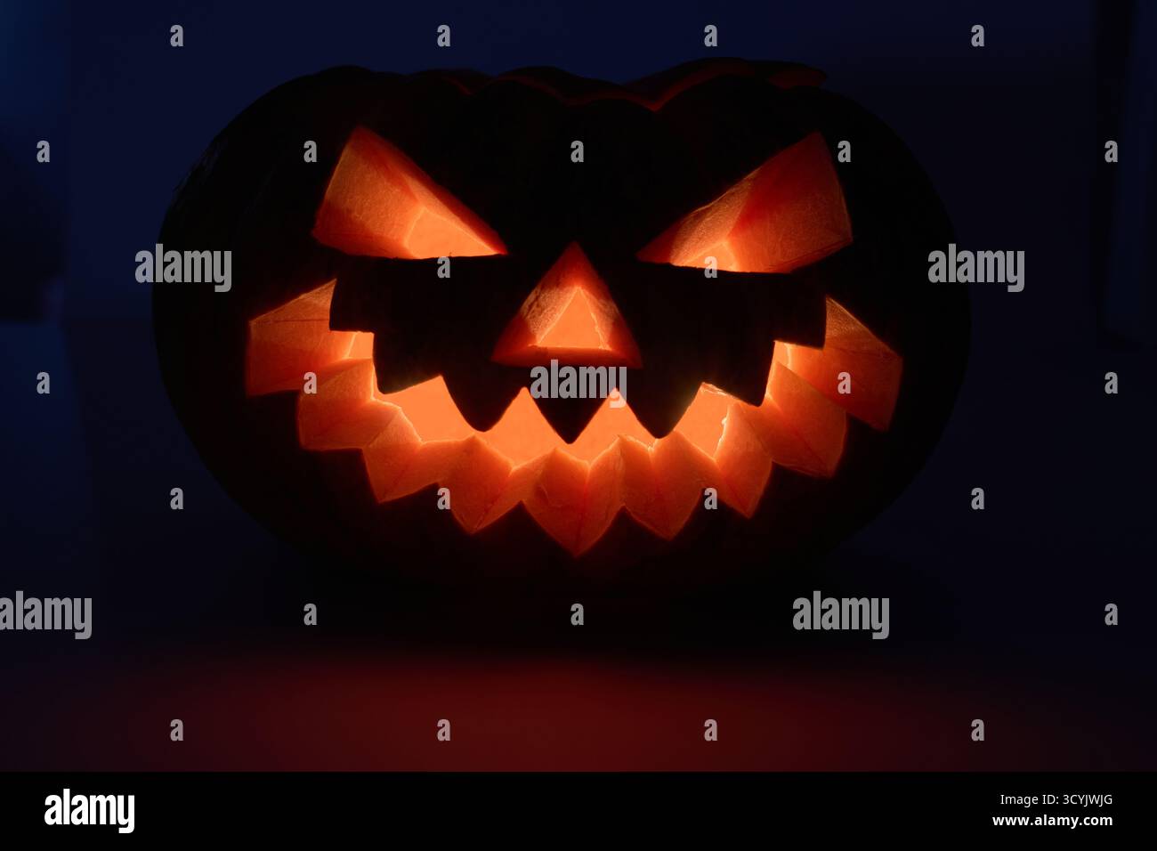 Une citrouille sculptée avec un visage de jack-o'-lanterne incandescent est illuminée sur un fond sombre Banque D'Images