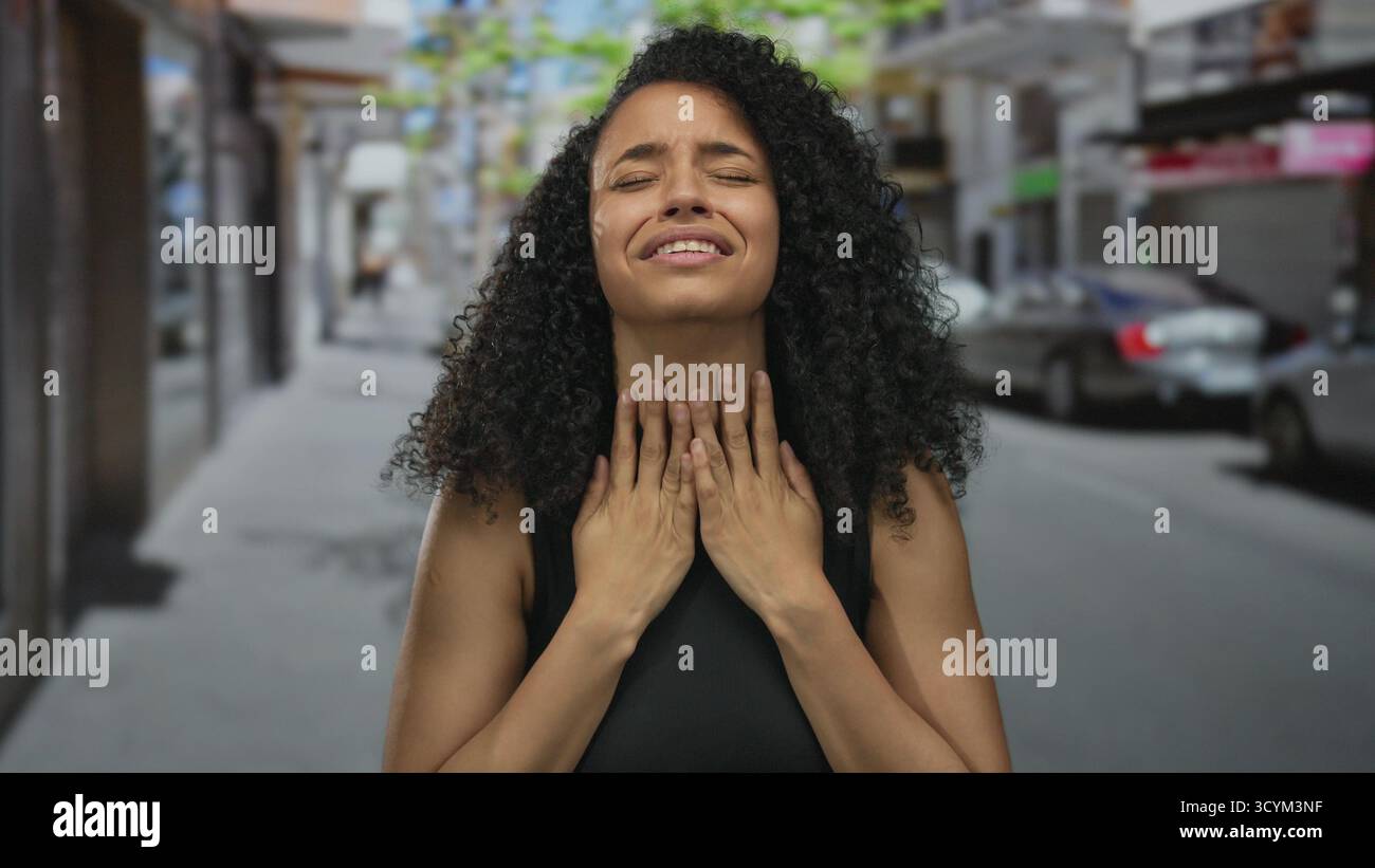 Femme en détresse dans la rue urbaine pendant la journée capture l'intensité émotionnelle dans un cadre public avec des cheveux bouclés et des vêtements sombres reflétant exp inquiet Banque D'Images