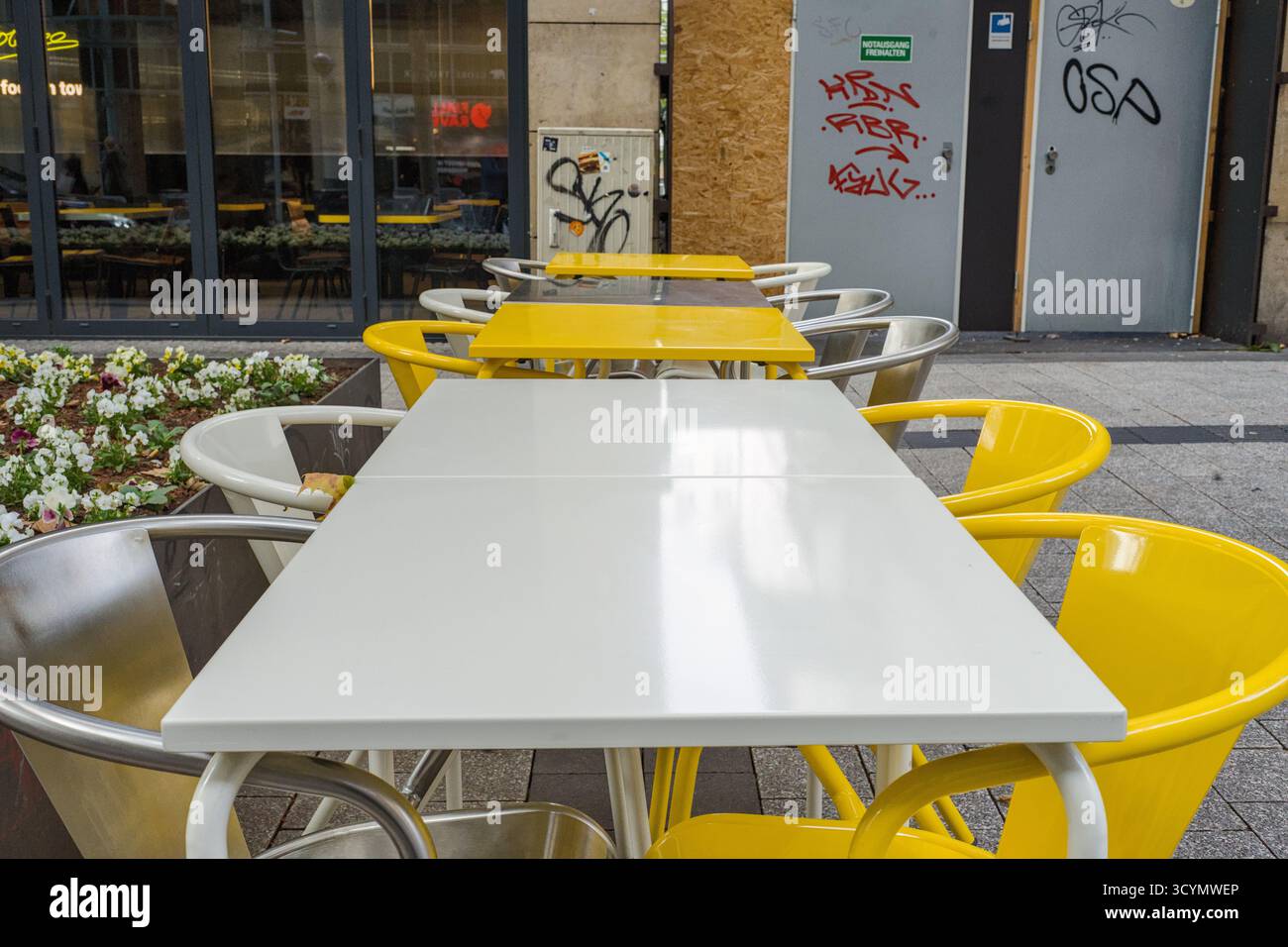 Tables et chaises jaunes et blanches d'un bistrot dans une zone piétonne d'une ville allemande, créant un coin salon extérieur lumineux et accueillant. Banque D'Images