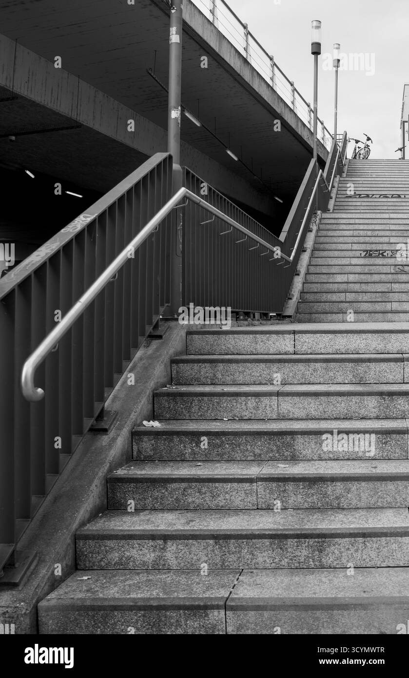 Photo en noir et blanc d'un escalier urbain menant vers le haut à un niveau de rue plus élevé, soulignant les lignes, le contraste et la perspective. Banque D'Images
