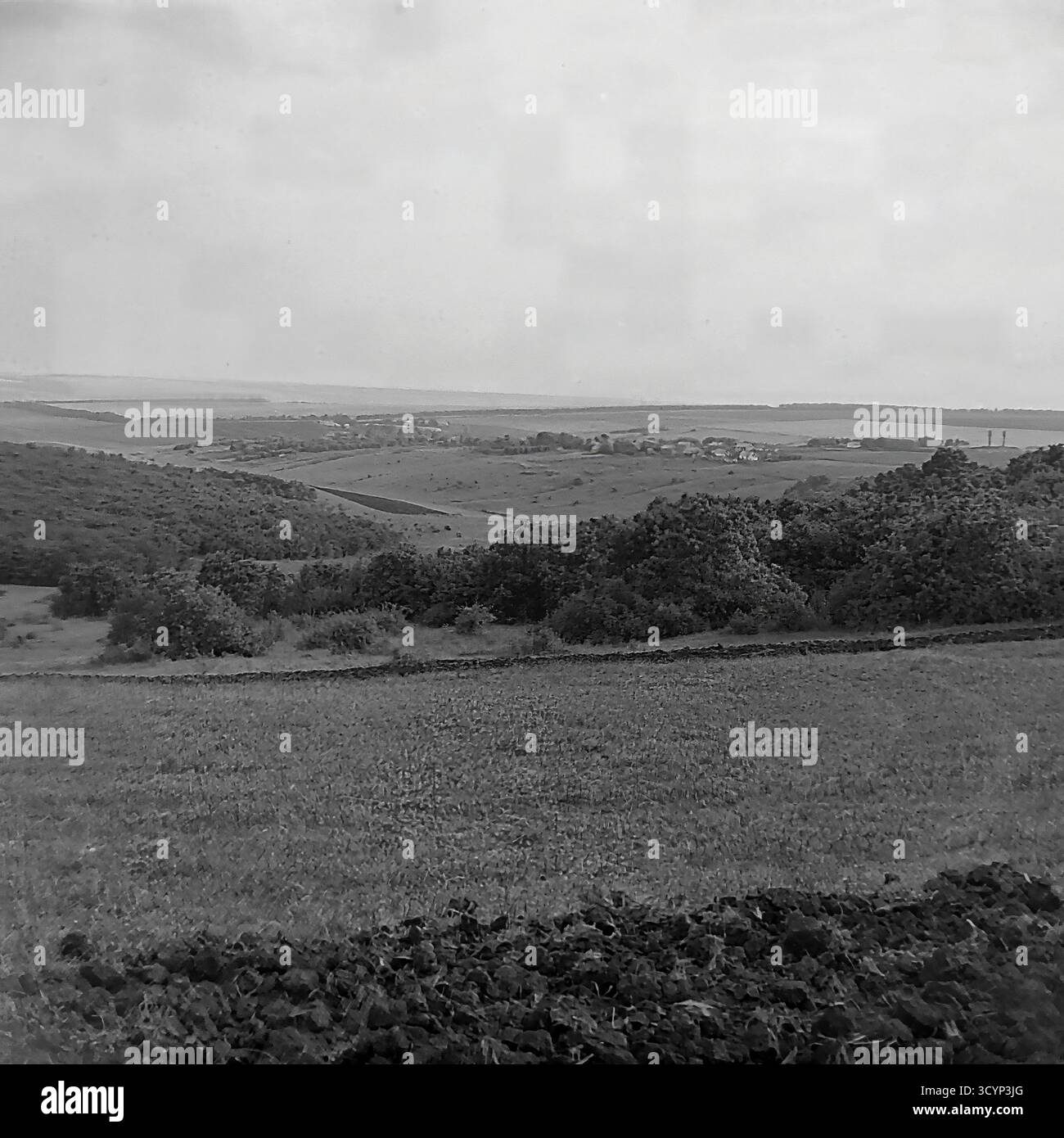 Cette photo d'archive des années 1970 montre une vue panoramique à angle élevé époustouflante du paysage rural près de Mayaky, oblast de Donetsk, RSS d'Ukraine. La photo donne sur de vastes champs agricoles et des collines ondulantes. Au premier plan, la terre sombre et fraîchement labourée contraste avec une prairie herbeuse. Au loin, un petit village est visible, et au-delà, une grande étendue d'eau, probablement la rivière Siverskyi Donets, s'étend jusqu'à l'horizon. Cette image capture parfaitement la beauté pastorale et expansive de la campagne soviétique, un élément clé du Donbass paisible Banque D'Images