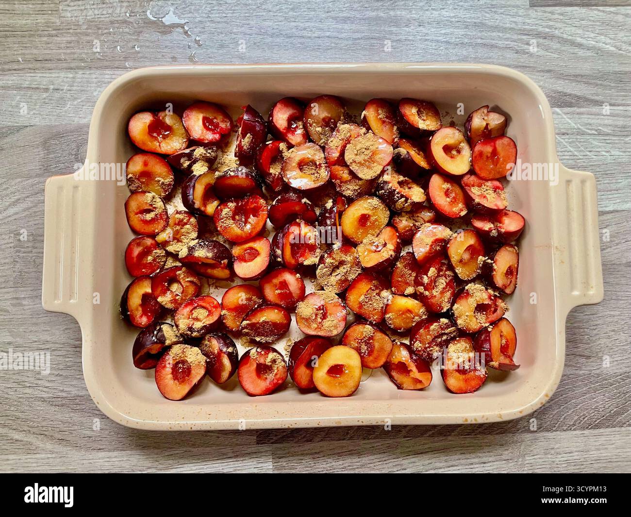 prunes coupées en deux recouvertes de sucre sur un plateau de bol à pâtisserie le creuset prêt à être rôti Banque D'Images