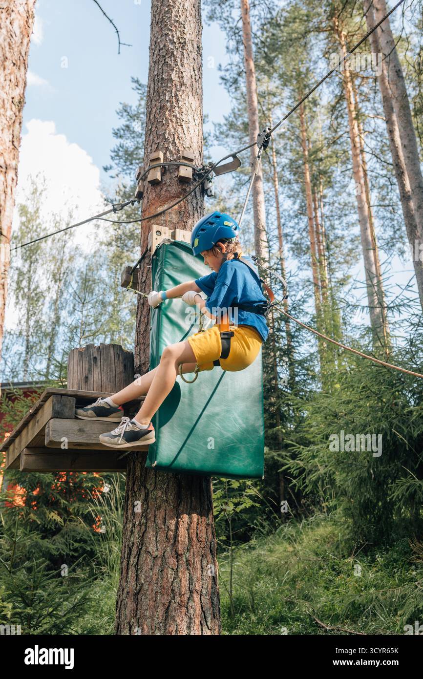 Garçon atterrissant sur la plate-forme rembourrée dans le cours de cordes hautes de forêt Banque D'Images