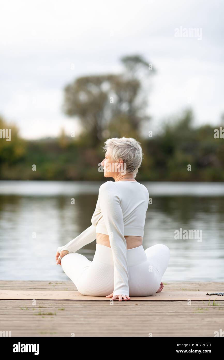 Une femme adulte en costume blanc pratique le yoga dans la nature. Il est assis en position de lotus avec son corps tourné sur le côté Banque D'Images