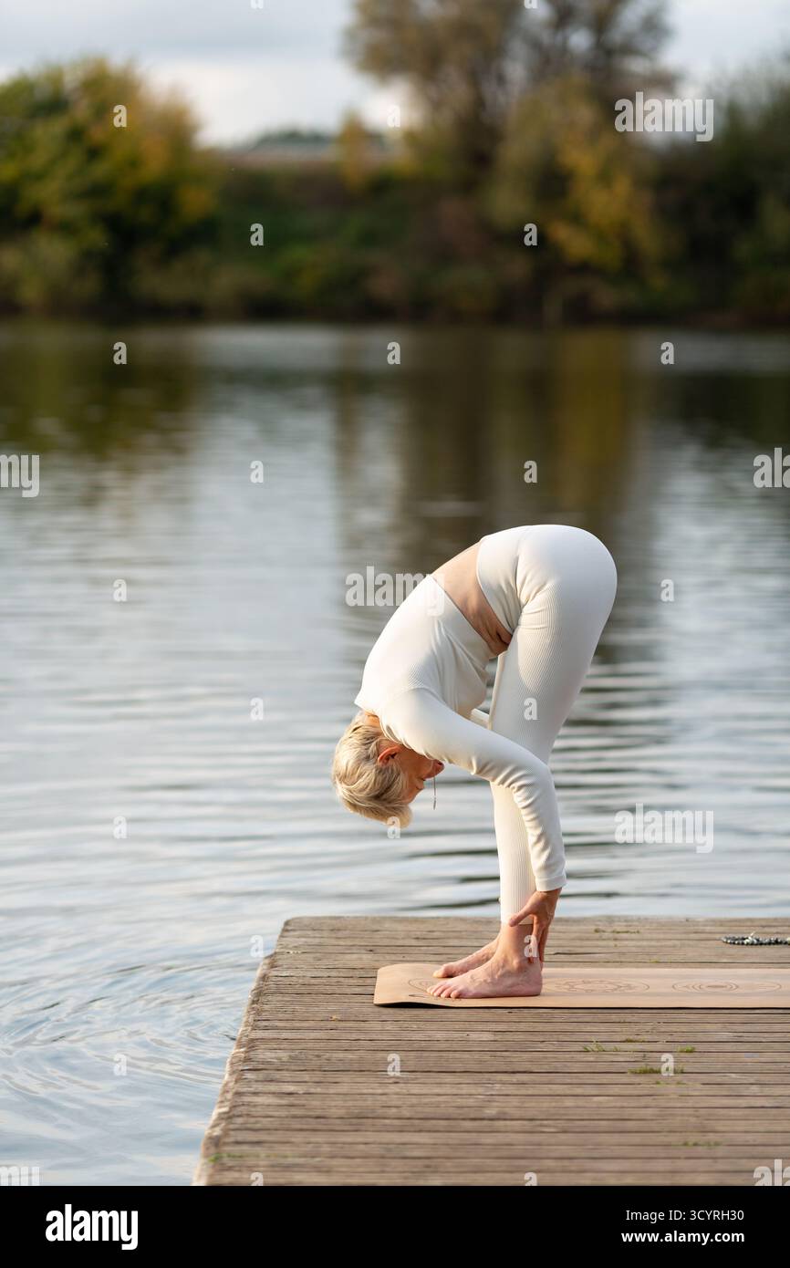 Une femme adulte en costume blanc pratique le yoga dans la nature. Il est assis en position de lotus avec son corps tourné sur le côté Banque D'Images