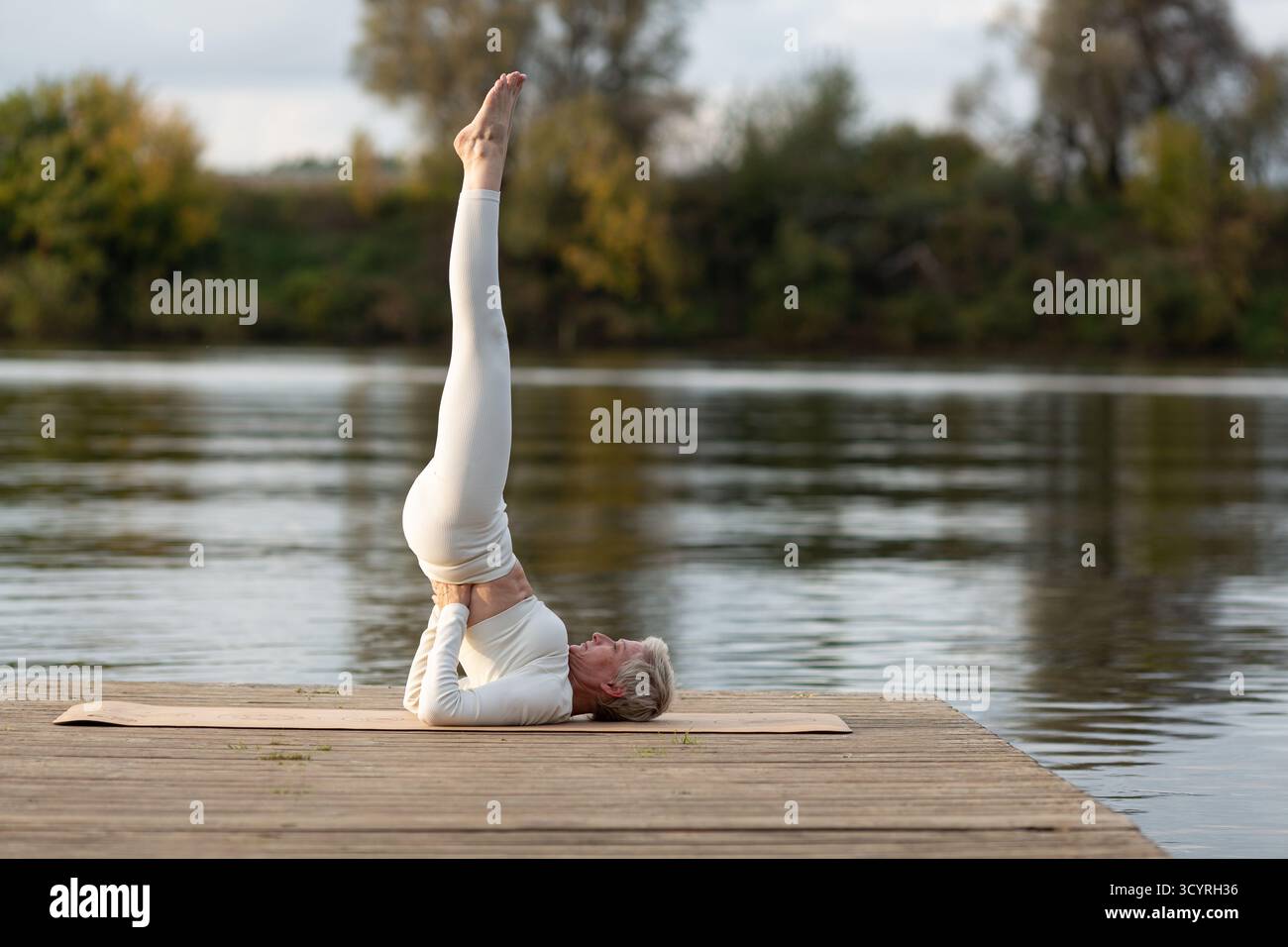 Une femme adulte en costume blanc pratique le yoga dans la nature. Il est assis en position de lotus avec son corps tourné sur le côté Banque D'Images