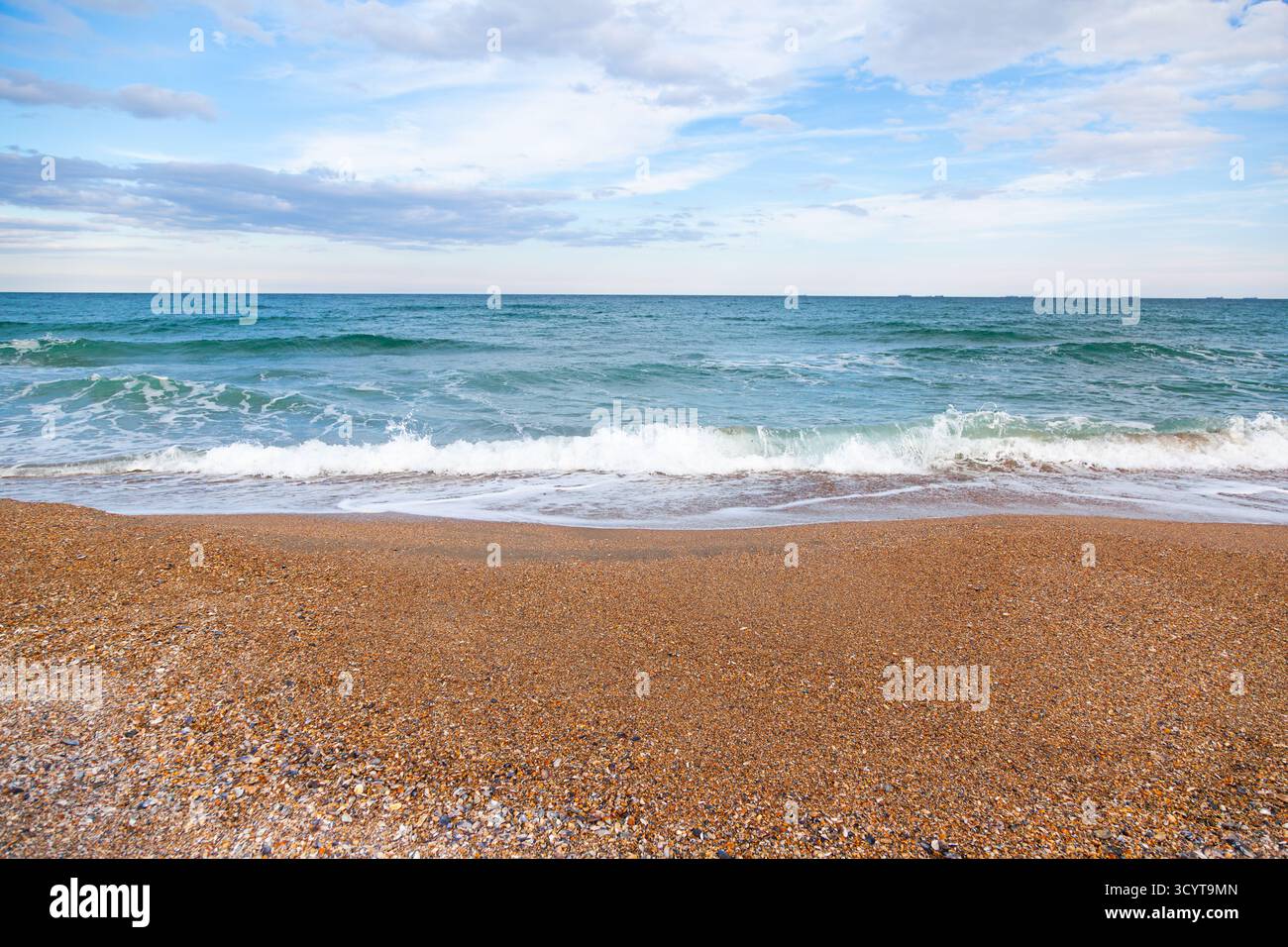 Côte d'une mer ondulée avec sable brun, coquillages et petits galets Banque D'Images