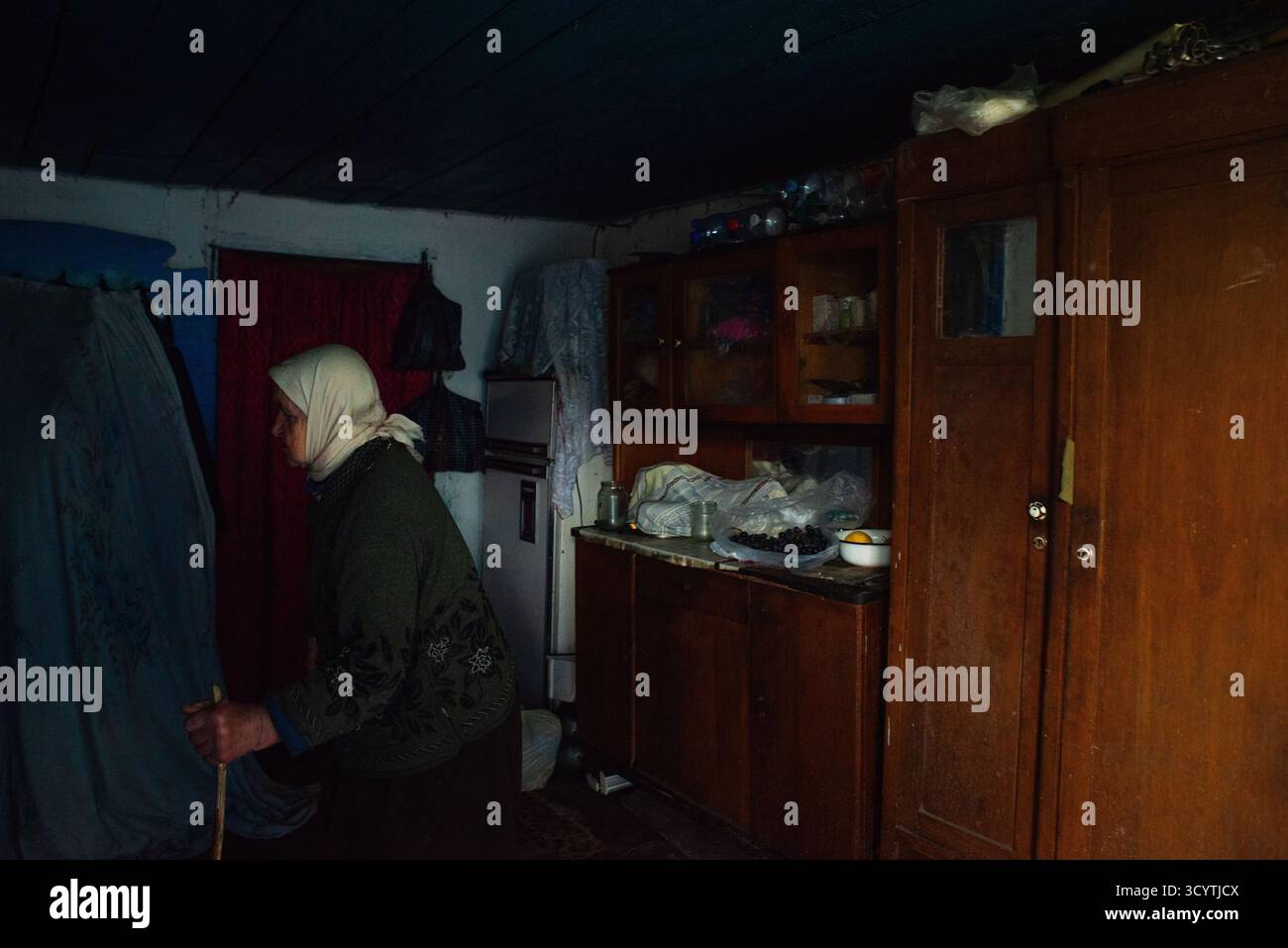 Une dame âgée solitaire avec un bâton de marche, avec de vieux meubles à l'arrière-plan Banque D'Images