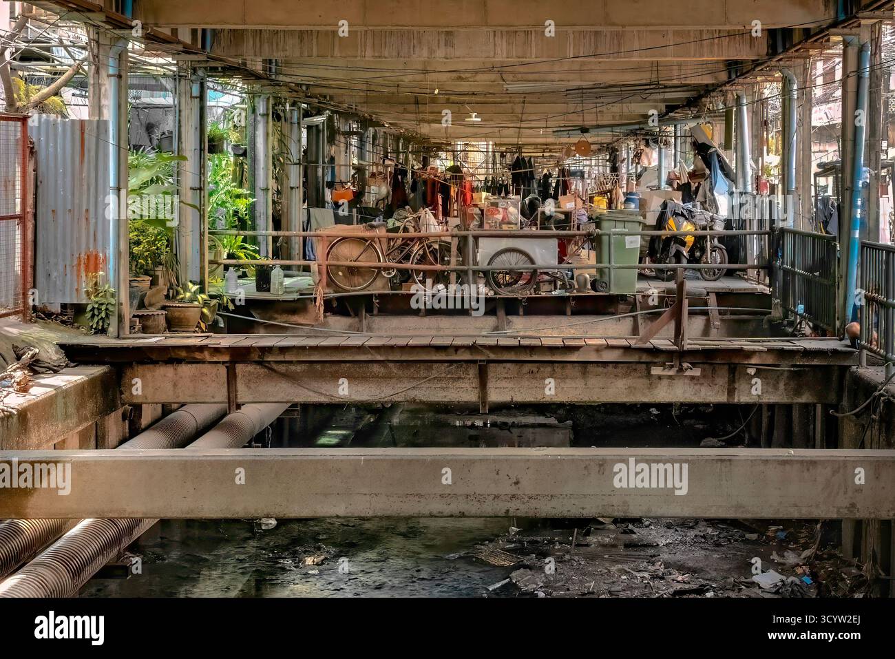 Décomposition urbaine sous une structure surélevée : une zone de stockage de fortune avec des vélos et de l'eau stagnante. Une vie de rue informelle au-dessus d'un cours d'eau. Banque D'Images
