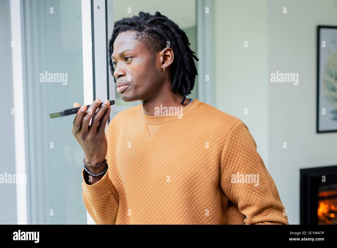 Homme afro-américain parlant dans le smartphone à l'intérieur du salon par porte coulissante à côté de la cheminée Banque D'Images