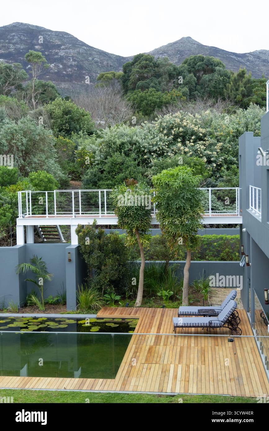 Piscine rectangulaire reflétant le ciel et abritant des nénuphars flottants à côté de chaises longues sur la terrasse Banque D'Images