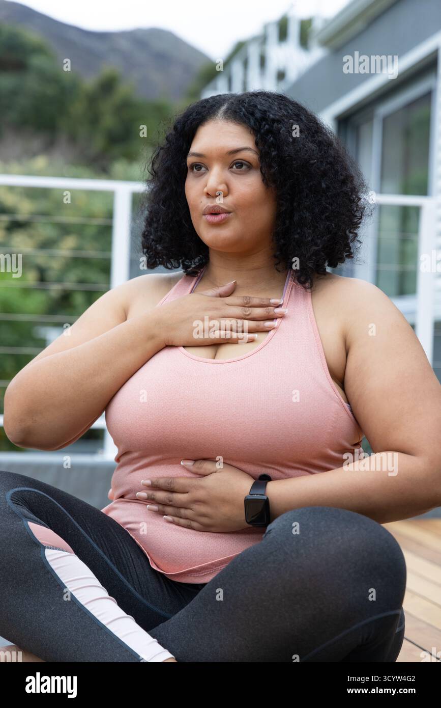 Femme afro-américaine assise sur le pont en bois pratiquant l'exercice de respiration dans le haut rose, smartwatch. Pleine conscience, bien-être, sérénité, plein air, relaxat Banque D'Images Femme afro-américaine assise sur le pont en bois pratiquant l'exercice de respiration dans le haut rose, smartwatch. Pleine conscience, bien-être, sérénité, plein air, relaxat Banque D'Images