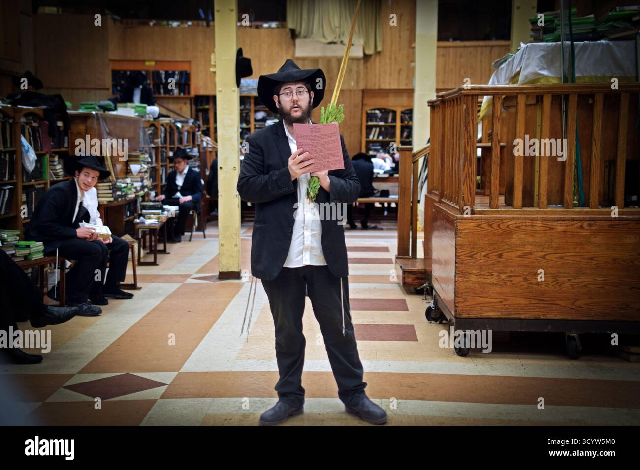 Sur Sukkos, un homme orthodoxe tenant une fronde de citron et de palmier dit une prière dans une synagogue. À Crown Heights, Brooklyn, New York. Banque D'Images