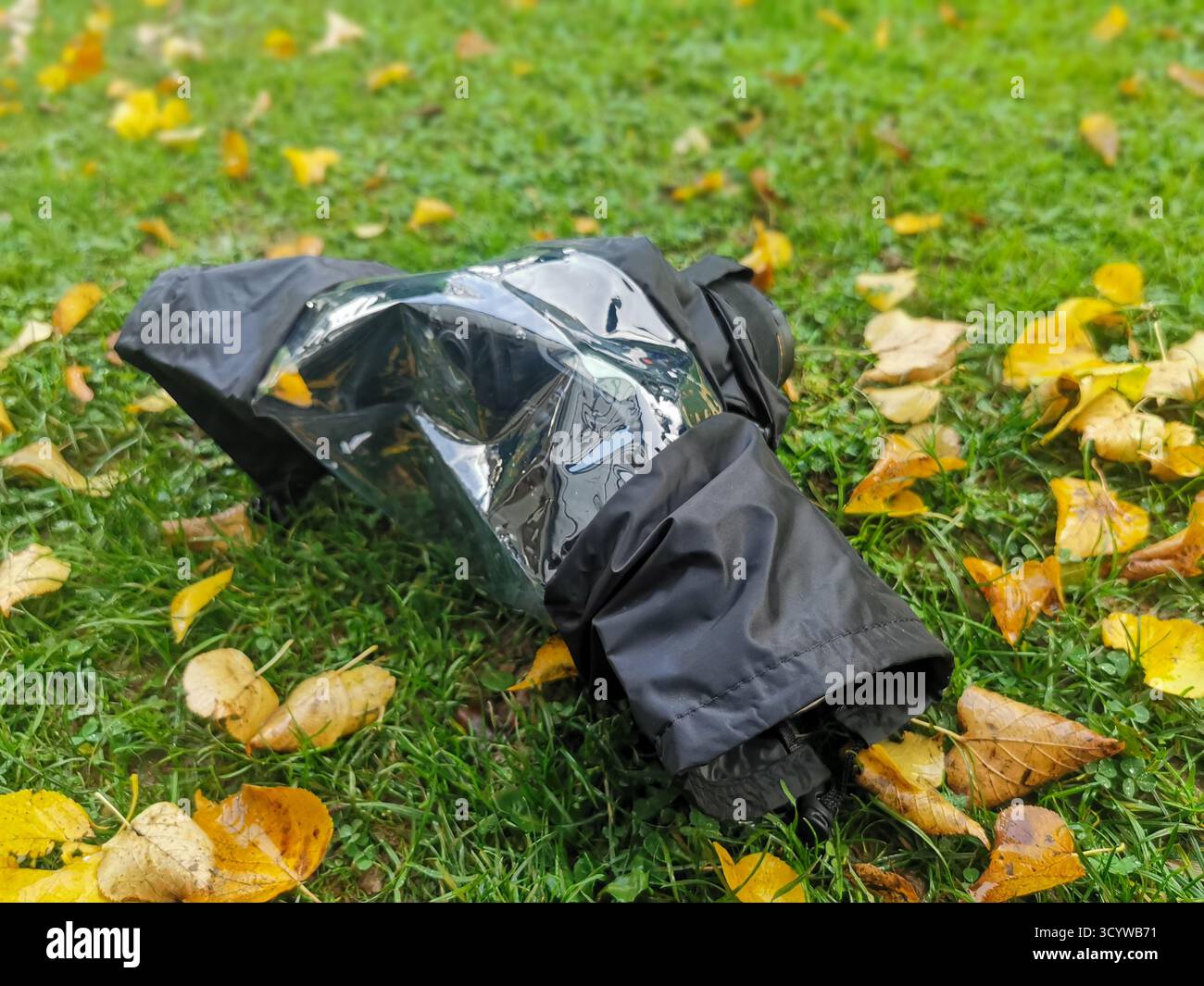 Sur une prairie se trouve un appareil photo dans une couverture de pluie. Les feuilles d'automne reposent sur l'herbe. En automne, protégez l'équipement de l'humidité et de la saleté. Banque D'Images