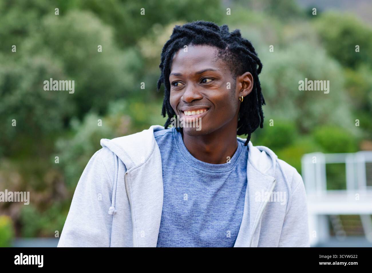 Homme afro-américain debout au parc près de la verdure et de la balustrade portant un sweat à capuche avec boucle d'oreille en or. Casual wear, outdoor, sérénité, naturel, lifestyle Banque D'Images Homme afro-américain debout au parc près de la verdure et de la balustrade portant un sweat à capuche avec boucle d'oreille en or. Casual wear, outdoor, sérénité, naturel, lifestyle Banque D'Images