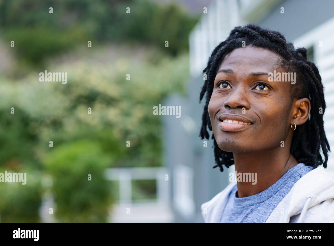 Homme afro-américain debout à côté d'un bâtiment gris en sweat à capuche regardant vers le haut les arbustes, espace de copie. Contemplation, urbain, minimalisme, nature, tranquille Banque D'Images Homme afro-américain debout à côté d'un bâtiment gris en sweat à capuche regardant vers le haut les arbustes, espace de copie. Contemplation, urbain, minimalisme, nature, tranquille Banque D'Images