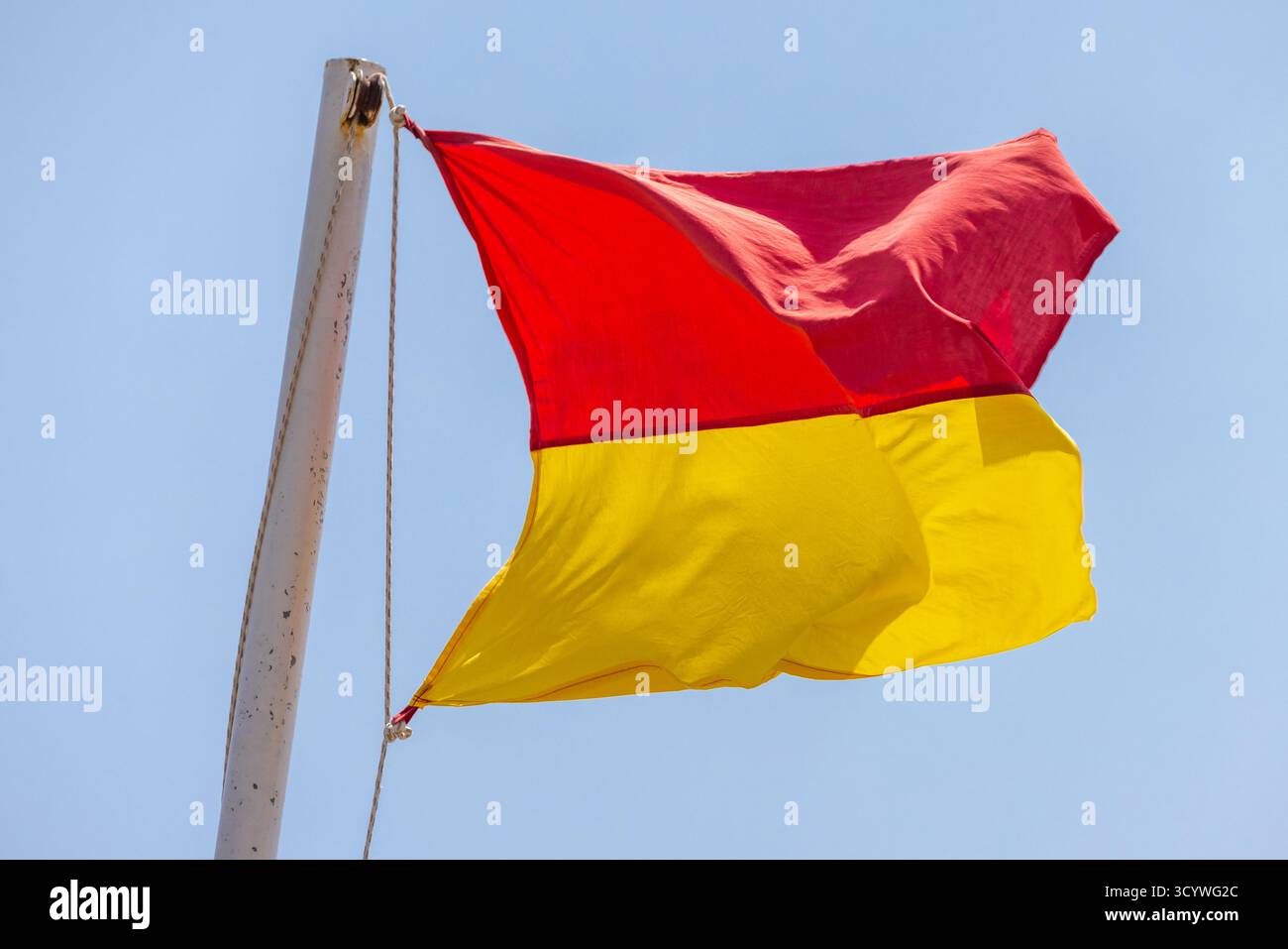 Drapeau rouge et jaune vif flambant sur un mât de drapeau blanc, placé contre un ciel bleu vif. Une image vivante et extérieure qui transmet l'énergie et le mouvement Banque D'Images Drapeau rouge et jaune vif flambant sur un mât de drapeau blanc, placé contre un ciel bleu vif. Une image vivante et extérieure qui transmet l'énergie et le mouvement Banque D'Images