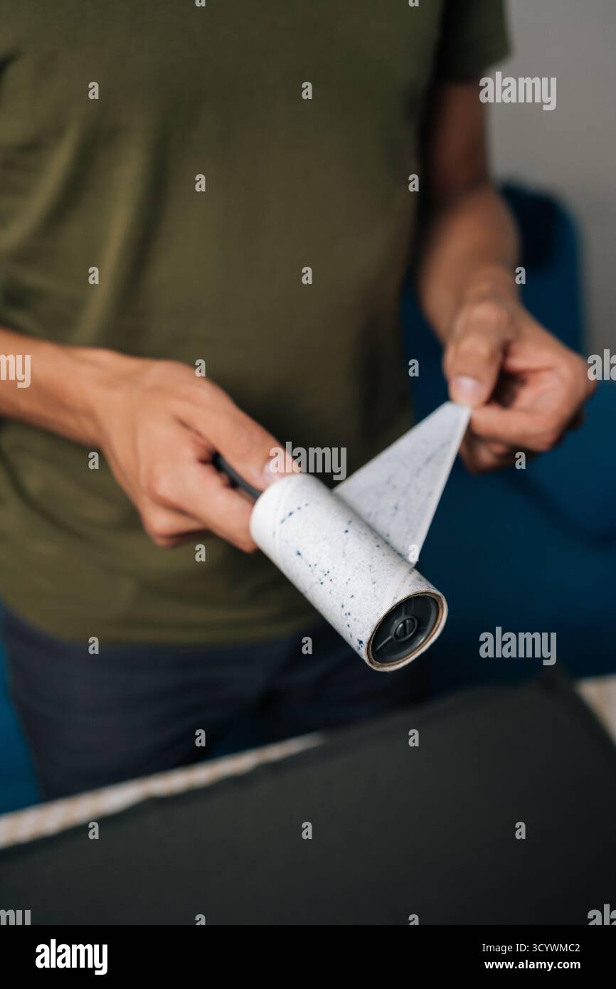 Plan vertical recadré de l'homme pelant la couche usagée de rouleau à peluches collantes, se préparant à nettoyer les vêtements de la poussière, des cheveux et des fibres, assurant des vêtements Banque D'Images