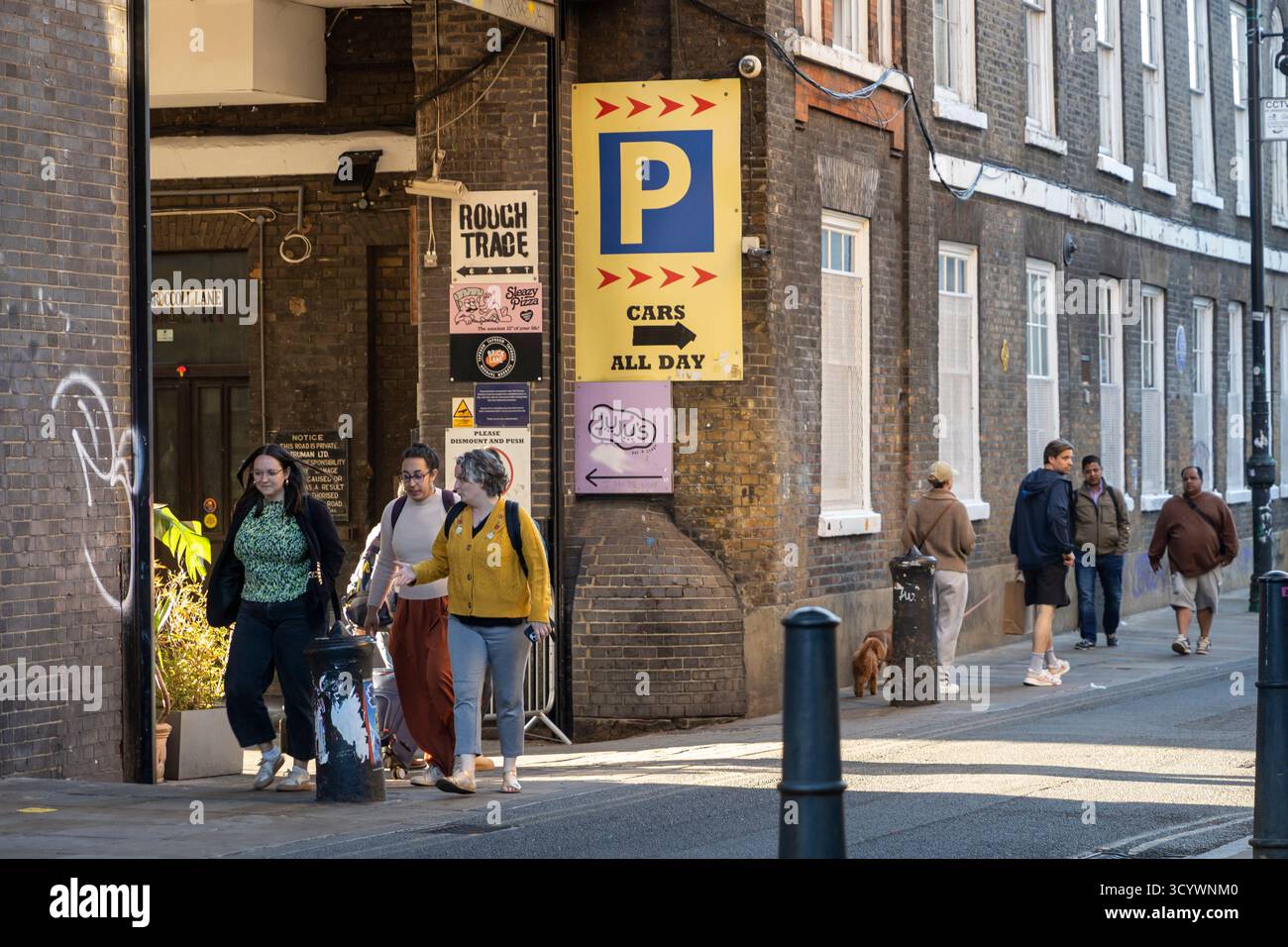 Londres, Royaume-Uni, 2 mai 2025. Les gens marchent devant une entrée commerciale rugueuse et une grande murale Street art à shoreditch Banque D'Images