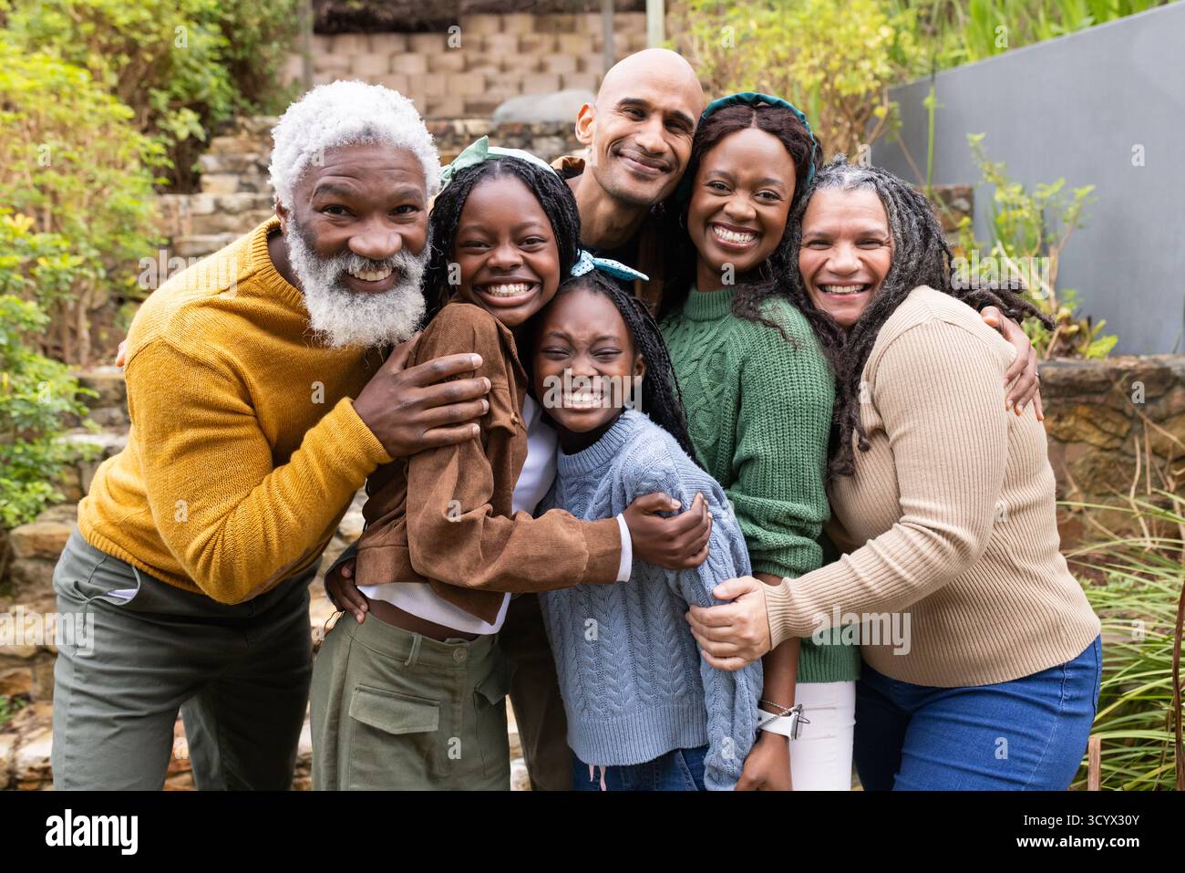Famille élargie diversifiée embrassant et souriant sur les marches de la terrasse du jardin avec murs de soutènement en pierre Banque D'Images