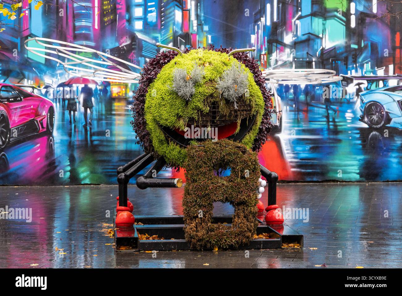 Installation d'art urbain d'une sculpture d'abeille géante faite de plantes sur un fond de graffiti de rue de néon dynamique Belfast Irlande du Nord Banque D'Images