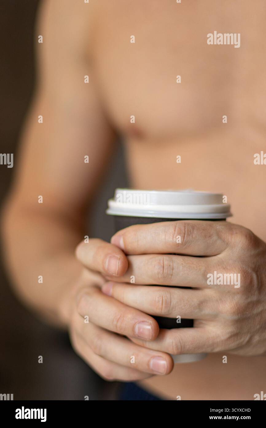 Mains tenant la tasse de café dans un moment calme. Gros plan de mains masculines berçant une tasse de café chaude, symbolisant la pause de travail à distance, rituel d'hygiène matinale Banque D'Images