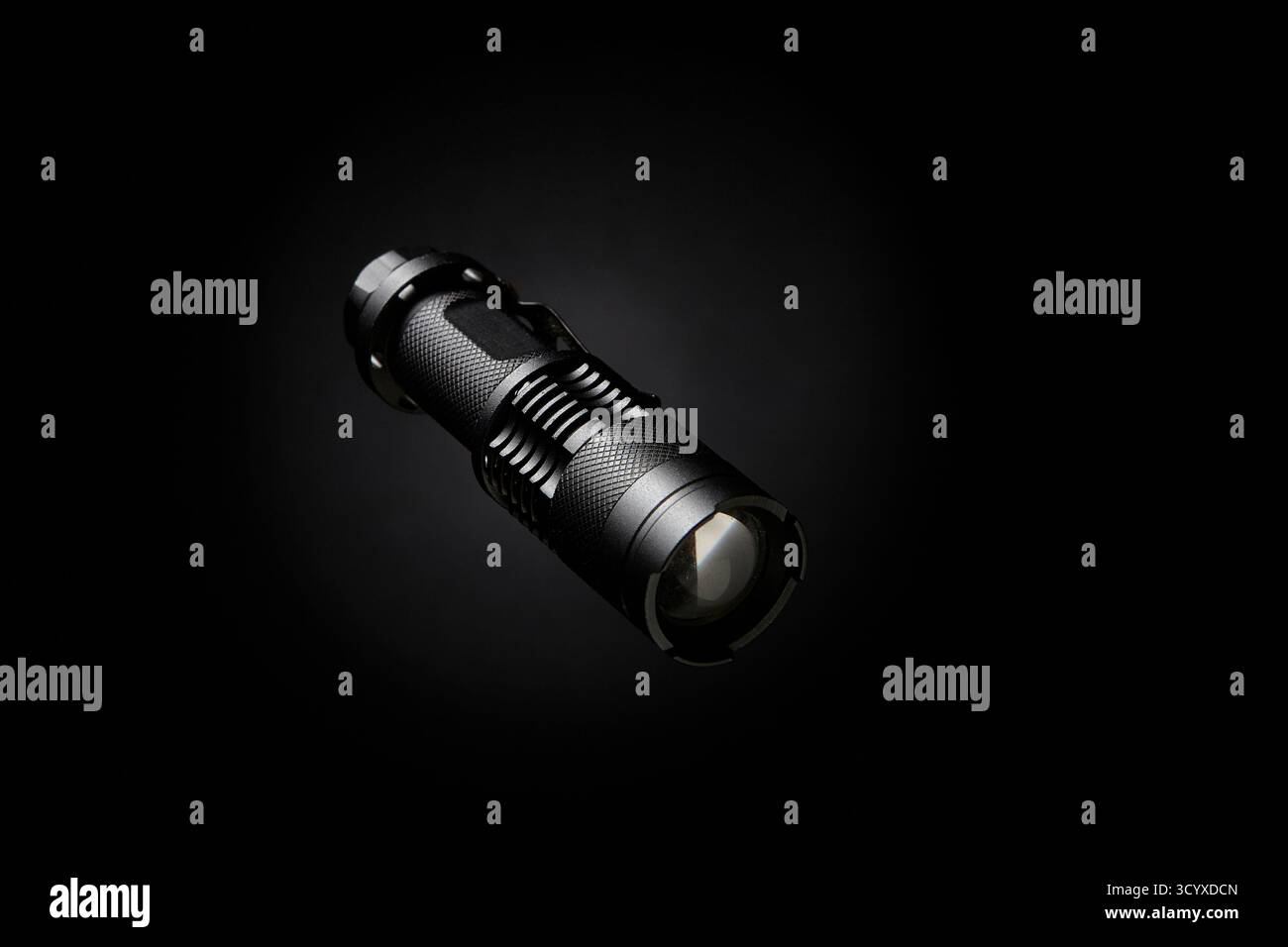 Image de produit professionnelle d'une lampe de poche tactique compacte avec réflexion claire de lentille. L'objet est centré sur un fond noir avec une lig dramatique Banque D'Images