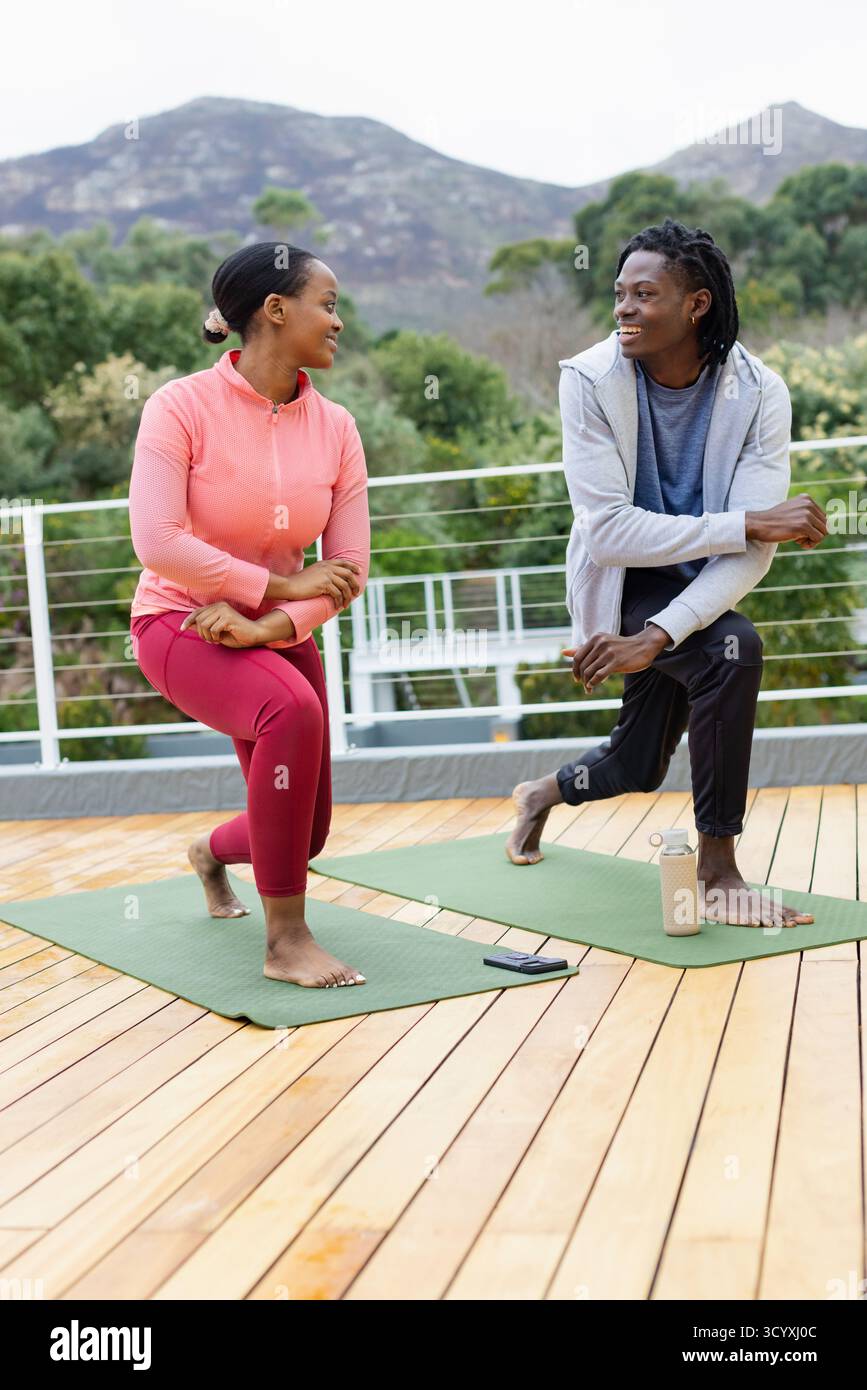 Amis afro-américains effectuant des fentes tordues sur le pont avec tapis de yoga smartphone bouteille d'eau. Fitness, entraînement en plein air, camaraderie, bien-être, AC Banque D'Images Amis afro-américains effectuant des fentes tordues sur le pont avec tapis de yoga smartphone bouteille d'eau. Fitness, entraînement en plein air, camaraderie, bien-être, AC Banque D'Images