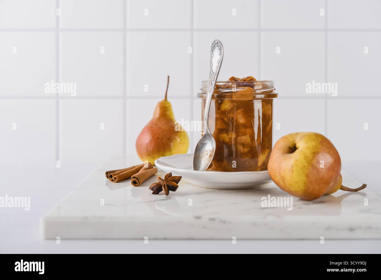 Confiture de poires dans un bocal en verre avec des poires mûres, des bâtonnets de cannelle et une cuillère à thé sur fond clair Banque D'Images