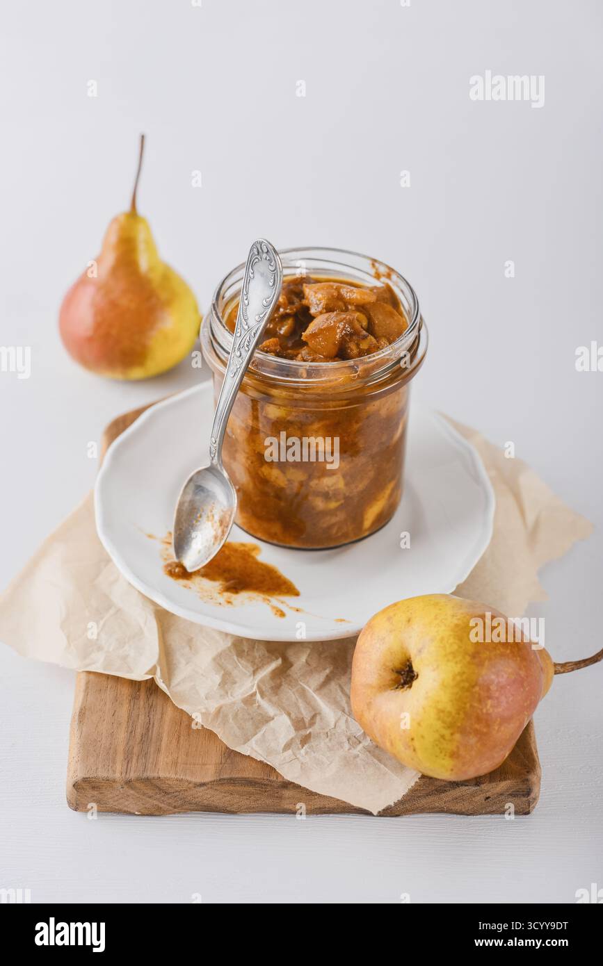 Confiture de poires dans un bocal en verre avec des poires mûres, des bâtonnets de cannelle et une cuillère à thé sur fond clair Banque D'Images