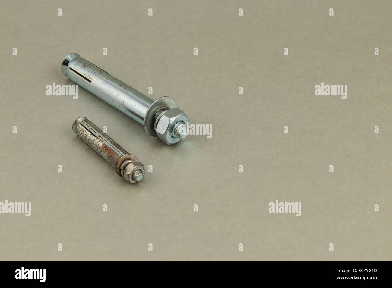Deux attaches métalliques reposent sur une surface plane. L'un est neuf et brillant, tandis que l'autre montre des signes d'usure. Idéal pour diverses tâches de construction ou de réparation Banque D'Images