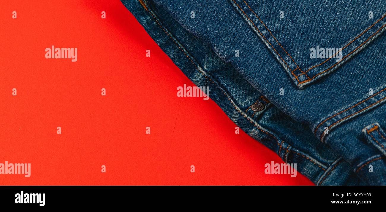 Les jeans denim sont soigneusement pliés et placés sur un fond rouge vif, créant un contraste visuel saisissant qui met en valeur leur style décontracté. Banque D'Images