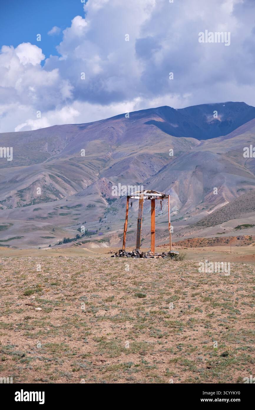 Construction religieuse en bois dans les montagnes de l'Altaï. Fait de poteaux et de pierres en bois. En arrière-plan chaîne de montagnes Kurai sous ciel bleu et nuages. Banque D'Images