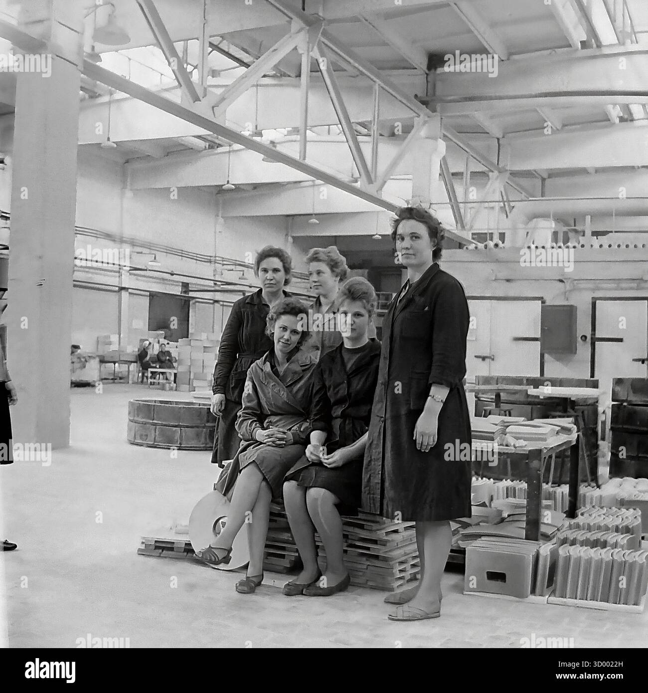 Cette photo d'archive de 1966 de Sloviansk, RSS d'Ukraine, montre un portrait de groupe de travailleuses à l'usine d'armature et d'isolateur (AIF). Cinq femmes, probablement une brigade, posent ensemble dans un atelier lumineux et spacieux. Ils sont habillés dans une tenue de travail simple. L'environnement propre et moderne, avec son haut plafond en treillis et des piles ordonnées de produits finis (éventuellement des carreaux de céramique), contraste avec les scènes typiques de l'industrie lourde. Cette image met en évidence le rôle des femmes et l'esprit collectif dans le travail soviétique, un document du Donbass pacifique Banque D'Images