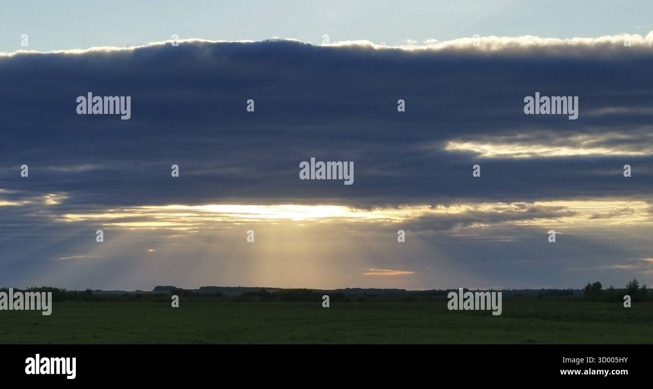 Le ciel est nuageux et le soleil se couche. Le soleil brille à travers les nuages, créant une atmosphère belle et sereine Banque D'Images