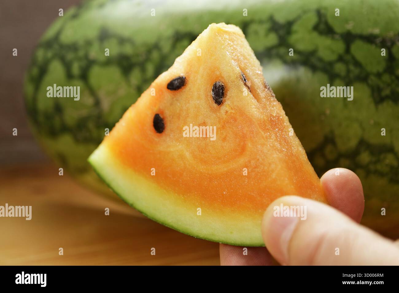 Gros plan d'une tranche de délicieuse pastèque orange avec le fruit entier en toile de fond Banque D'Images
