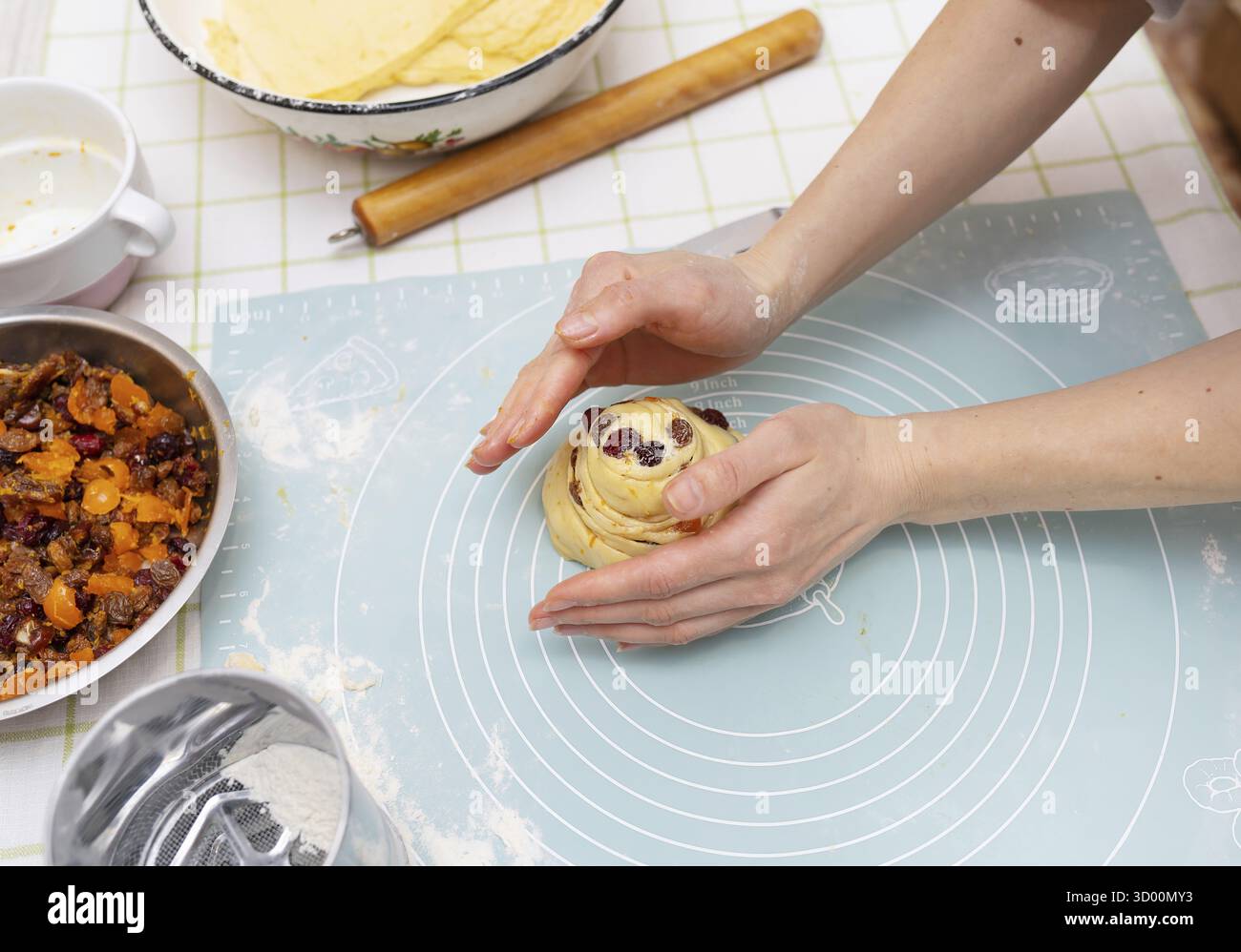 Les mains d'une jeune femme caucasienne façonnent soigneusement un pain de Pâques sucré, rempli de fruits secs. La pâtisserie festive est presque prête pour la cuisson Banque D'Images
