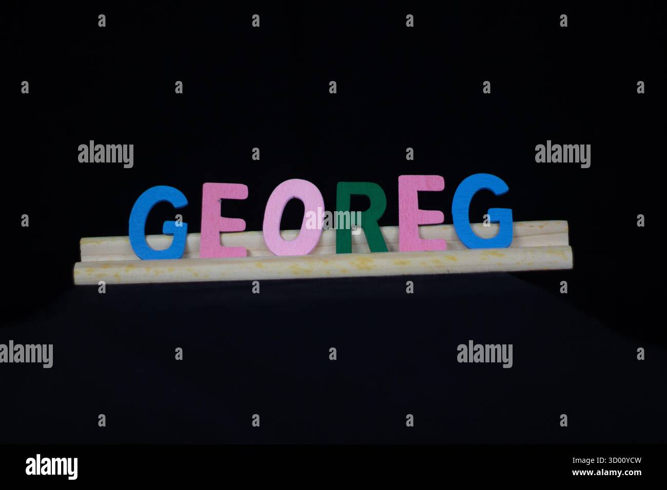 Nom de garçon traditionnel George en lettres en bois multicolores sur un support de tuiles isolé sur un fond noir Banque D'Images