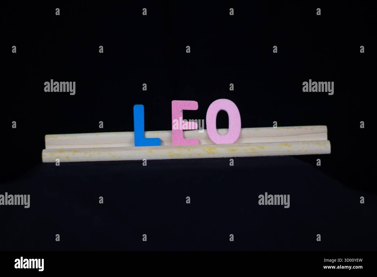 Nom de garçon traditionnel Leo en lettres en bois multicolores sur un support de tuiles isolé sur un fond noir Banque D'Images