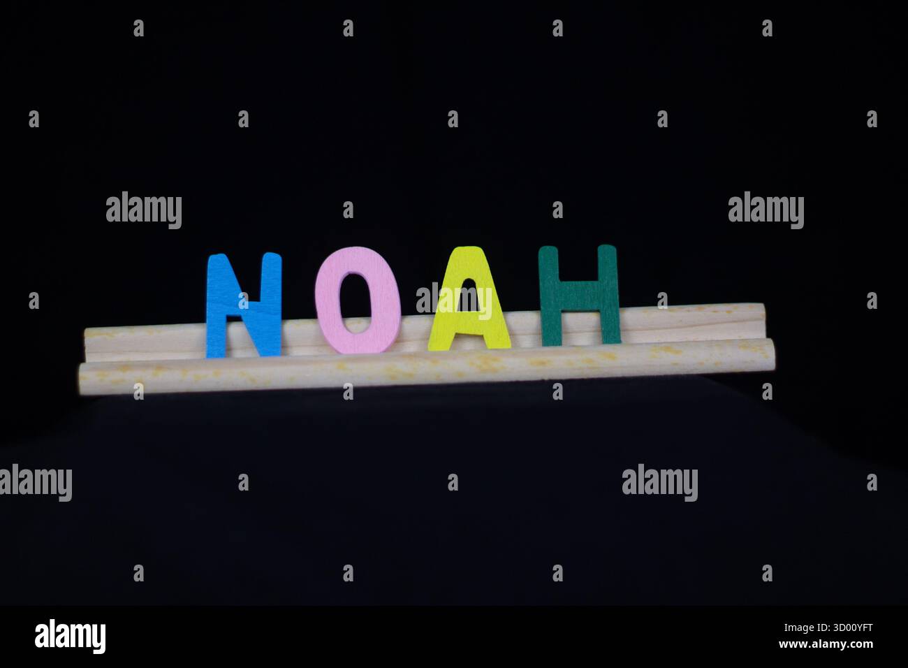 Noah nom de garçon traditionnel en lettres en bois multicolores sur un support de tuiles isolé sur un fond noir Banque D'Images