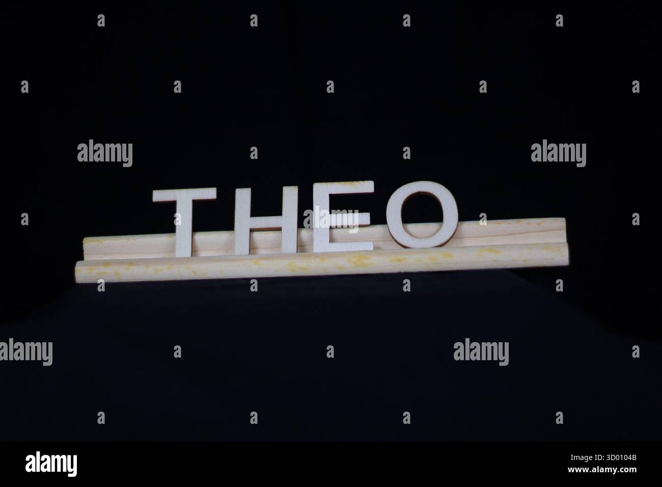 Theo nom traditionnel de garçon en lettres en bois ordinaire sur un support de tuiles isolé sur un fond noir Banque D'Images