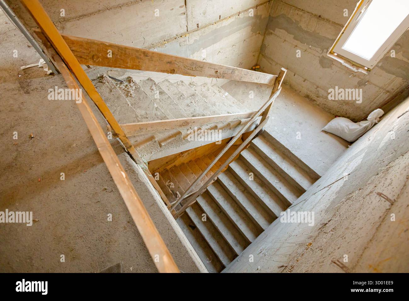 Nouvel escalier en béton inachevé avec temporaire, improvisé comme mesure de sécurité, la main courante en bois descend, en construction. Banque D'Images