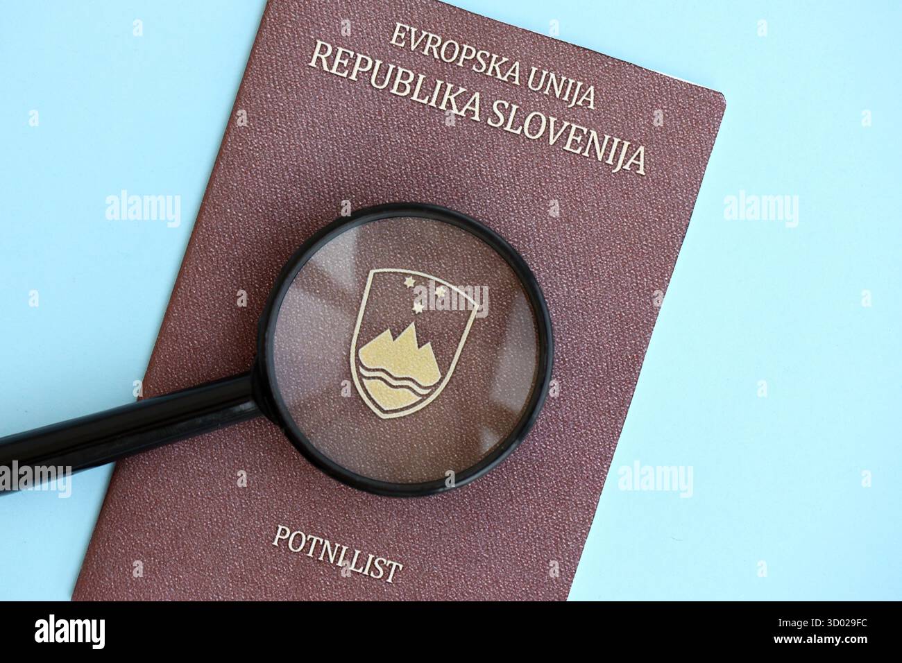 Passeport slovène et loupe sur fond de papier bleu clair gros plan. Détails de citoyenneté et concept d'information Banque D'Images